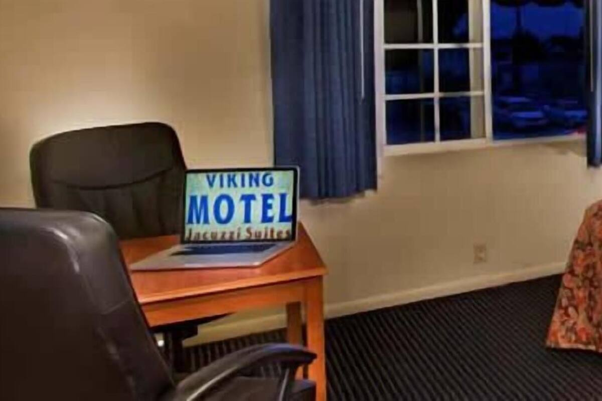 A hotel room with a bed, a desk with a computer, a chair, a lamp, and a sign indicating it's a Viking Motel.