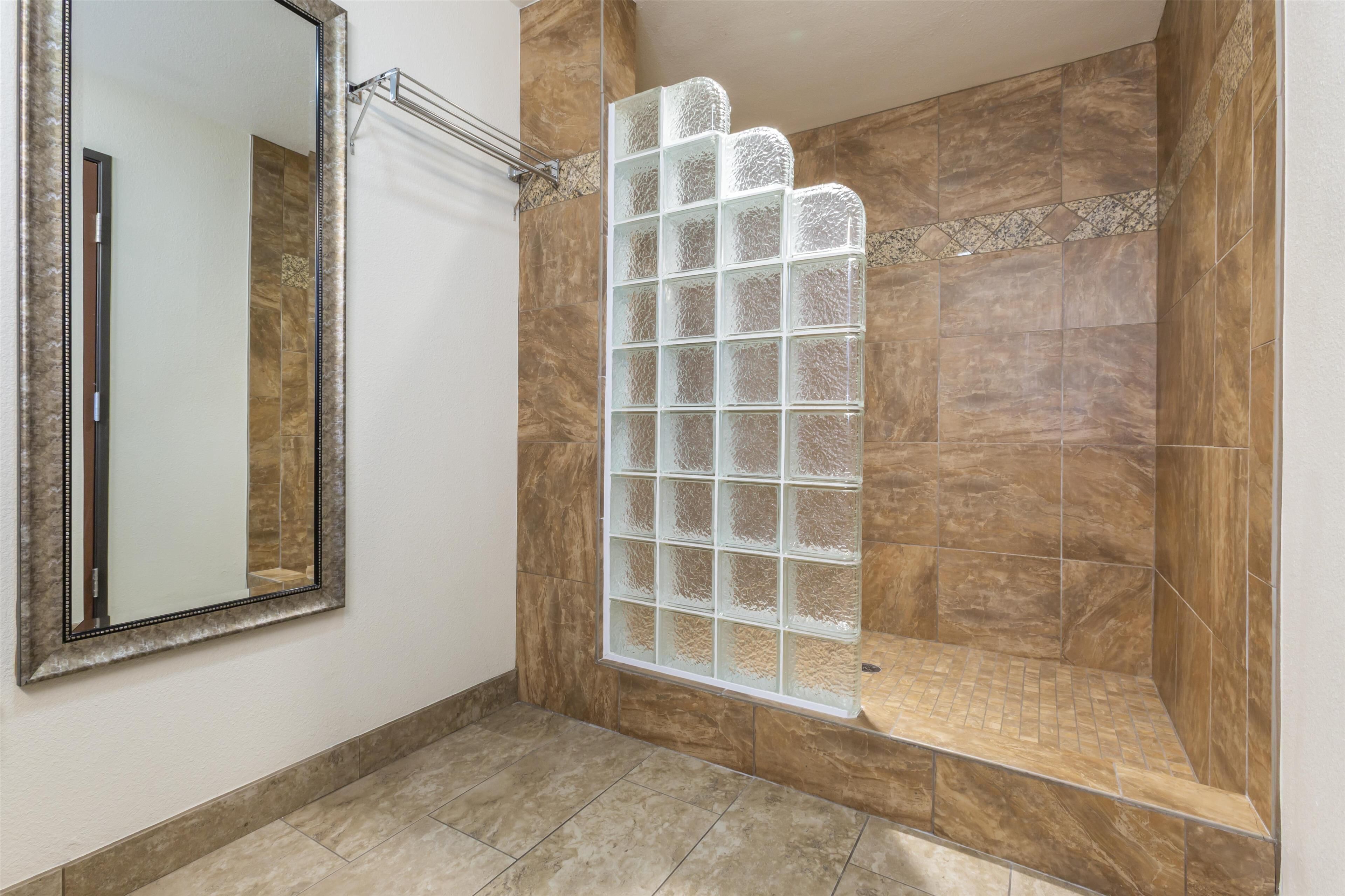 A bathroom with a large mirror, a shower with a glass door, and tiled walls.