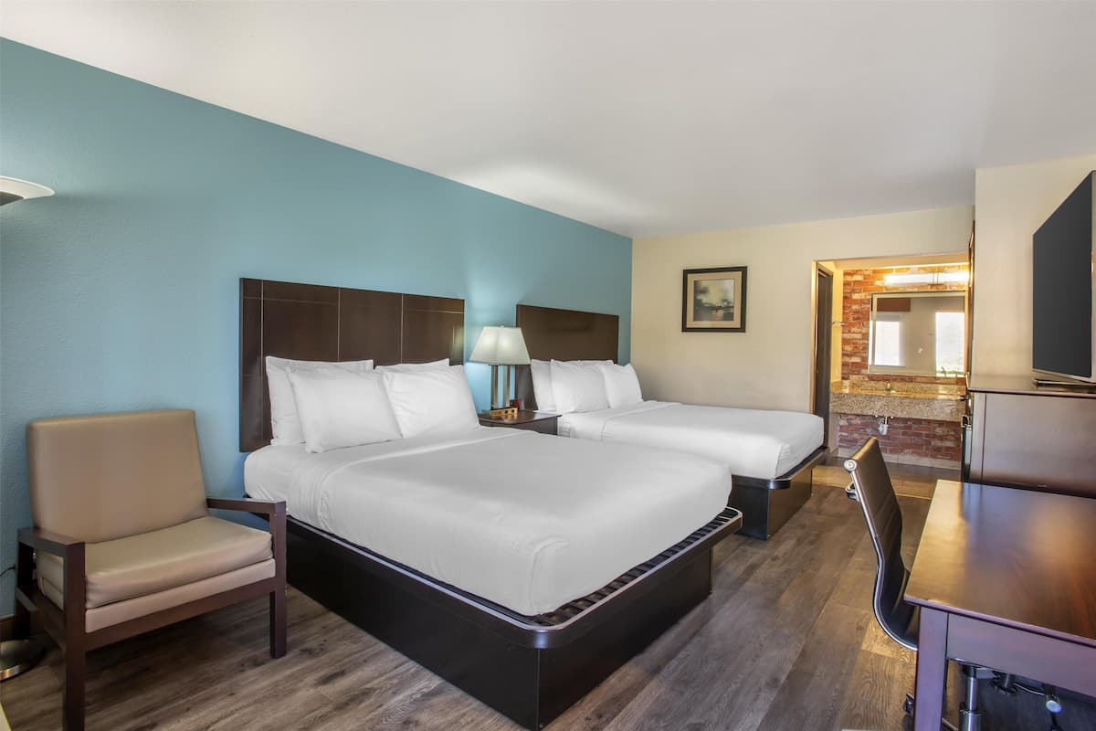 A hotel room with two beds, a desk, a chair, a lamp, and a TV.