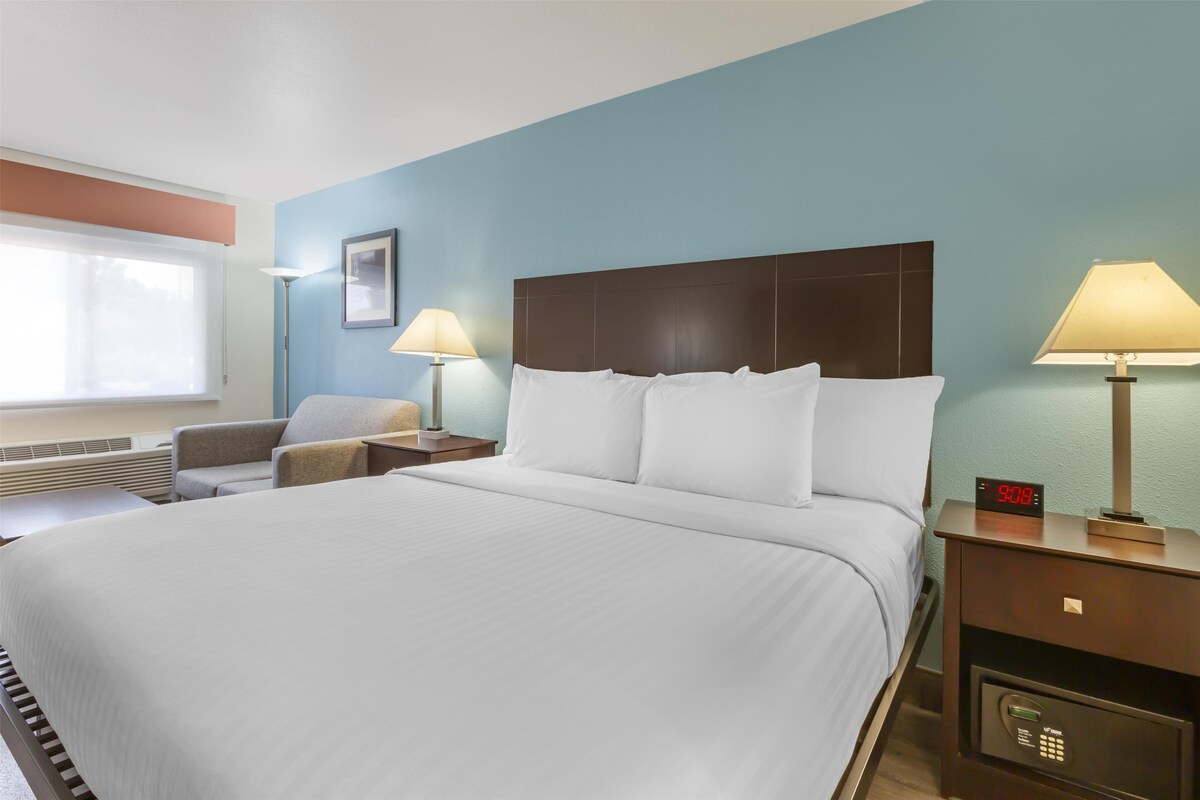 A hotel room with a large bed, two bedside tables with lamps, a clock, and a chair.