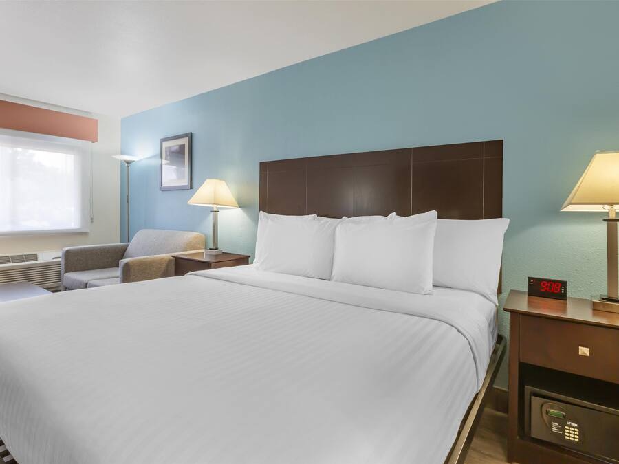 Une chambre d’hôtel avec un grand lit, deux tables de chevet avec des lampes, une horloge et une chaise.