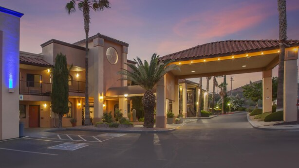 A hotel entrance with a covered walkway, palm trees, and a clock tower. - Best Western Copper Hills Inn (Globe)