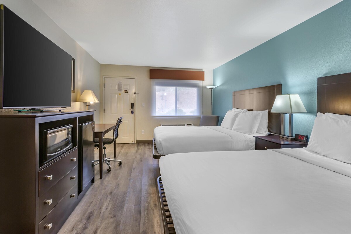 A hotel room with two beds, a desk with a computer, a microwave, and a TV.