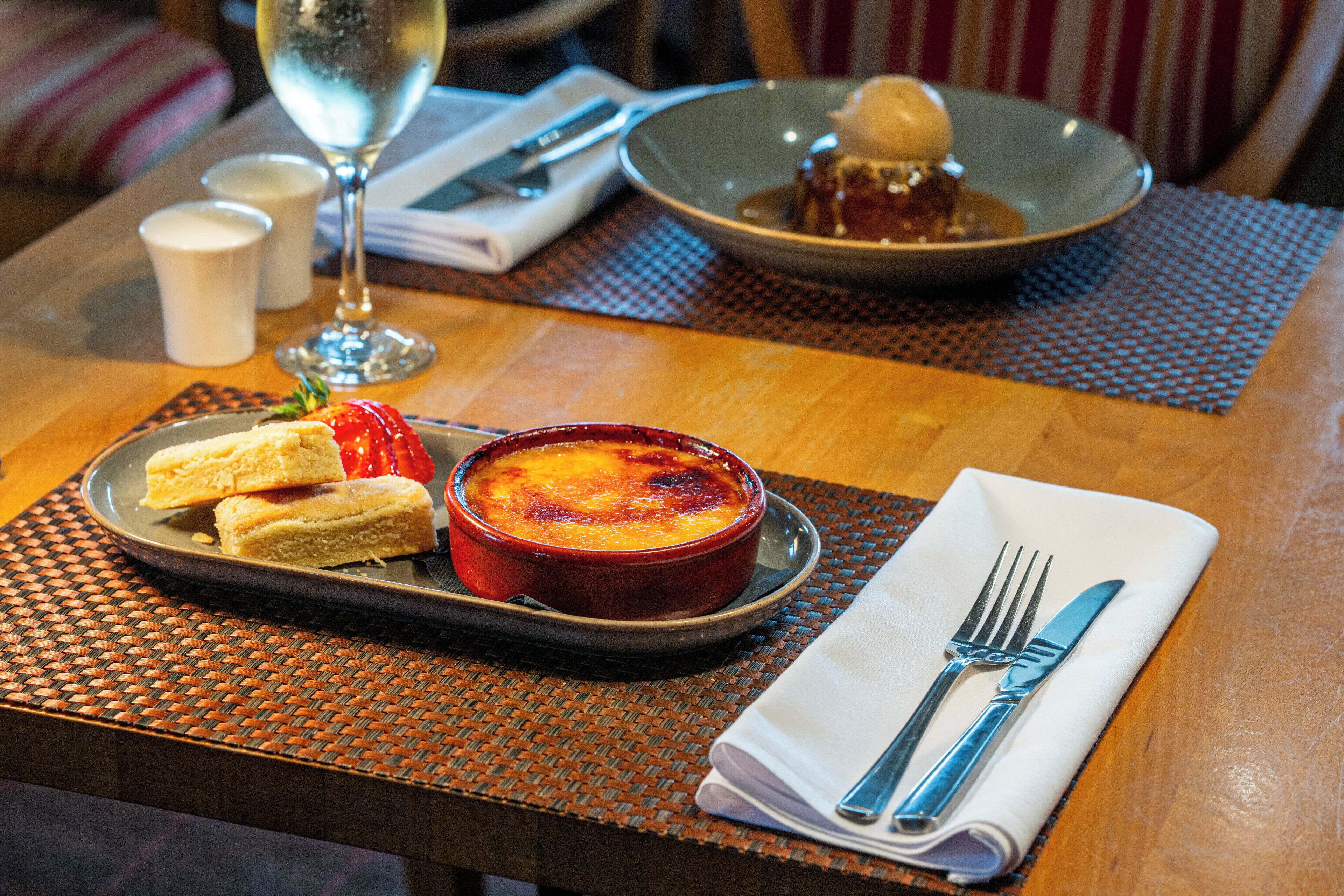 A dining table with a dessert plate, a bowl of soup, and a glass of wine.