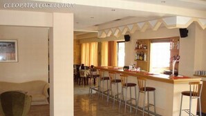 Un bar d’hôtel doté d’un long comptoir, de plusieurs tabourets et d’un espace salon avec un canapé et des fauteuils.