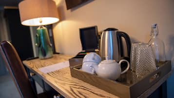 A wooden tray with a teapot, a kettle, a glass jar, and a lamp on a table.