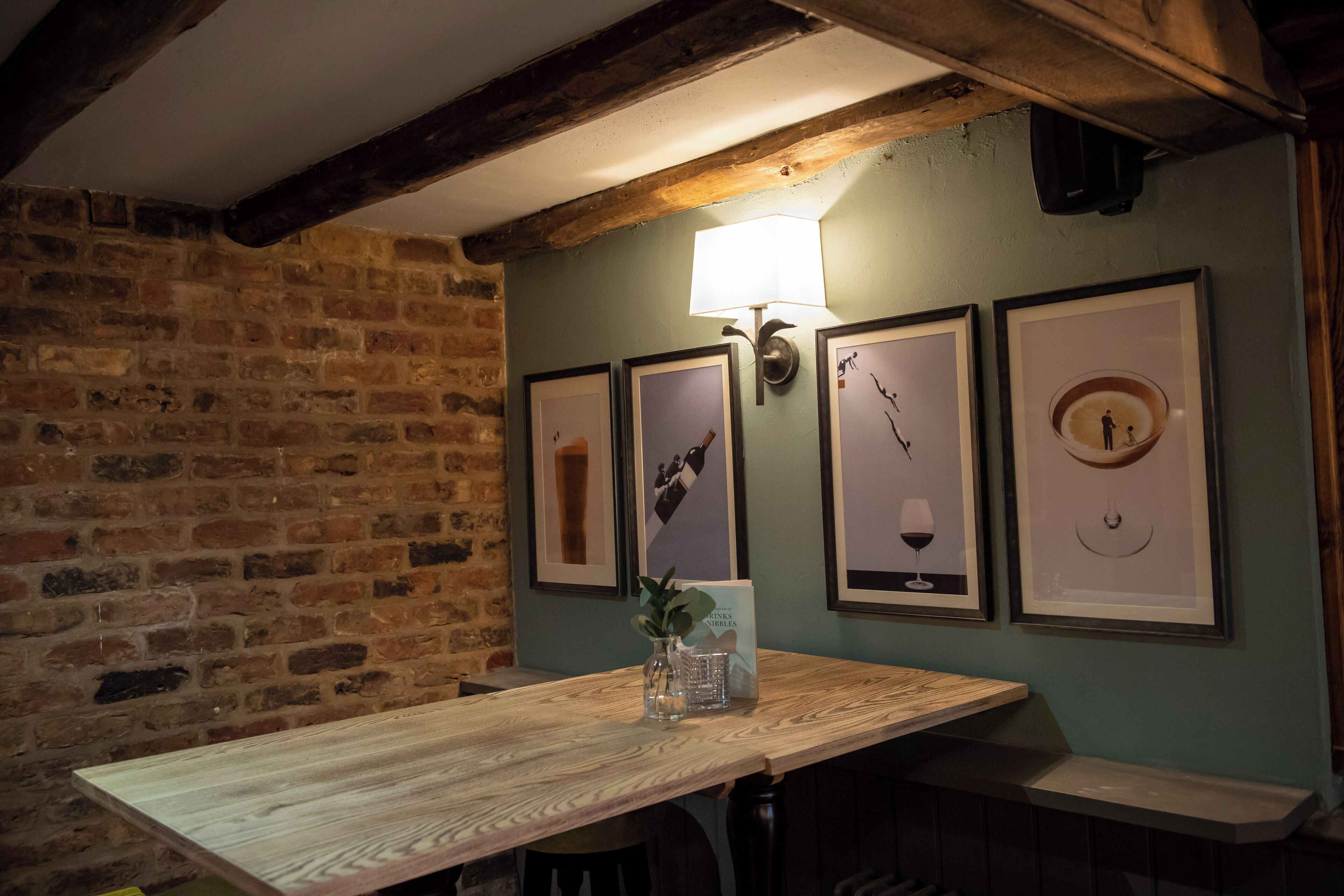A rustic room with exposed brick walls, a wooden table, and framed pictures on the wall.