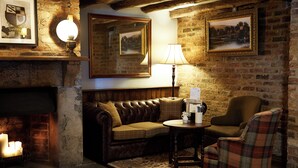 A cozy room with a fireplace, a leather sofa, a plaid armchair, and a table with a lamp. - Red Lion Todwick by Chef and Brewer Collection (Sheffield)