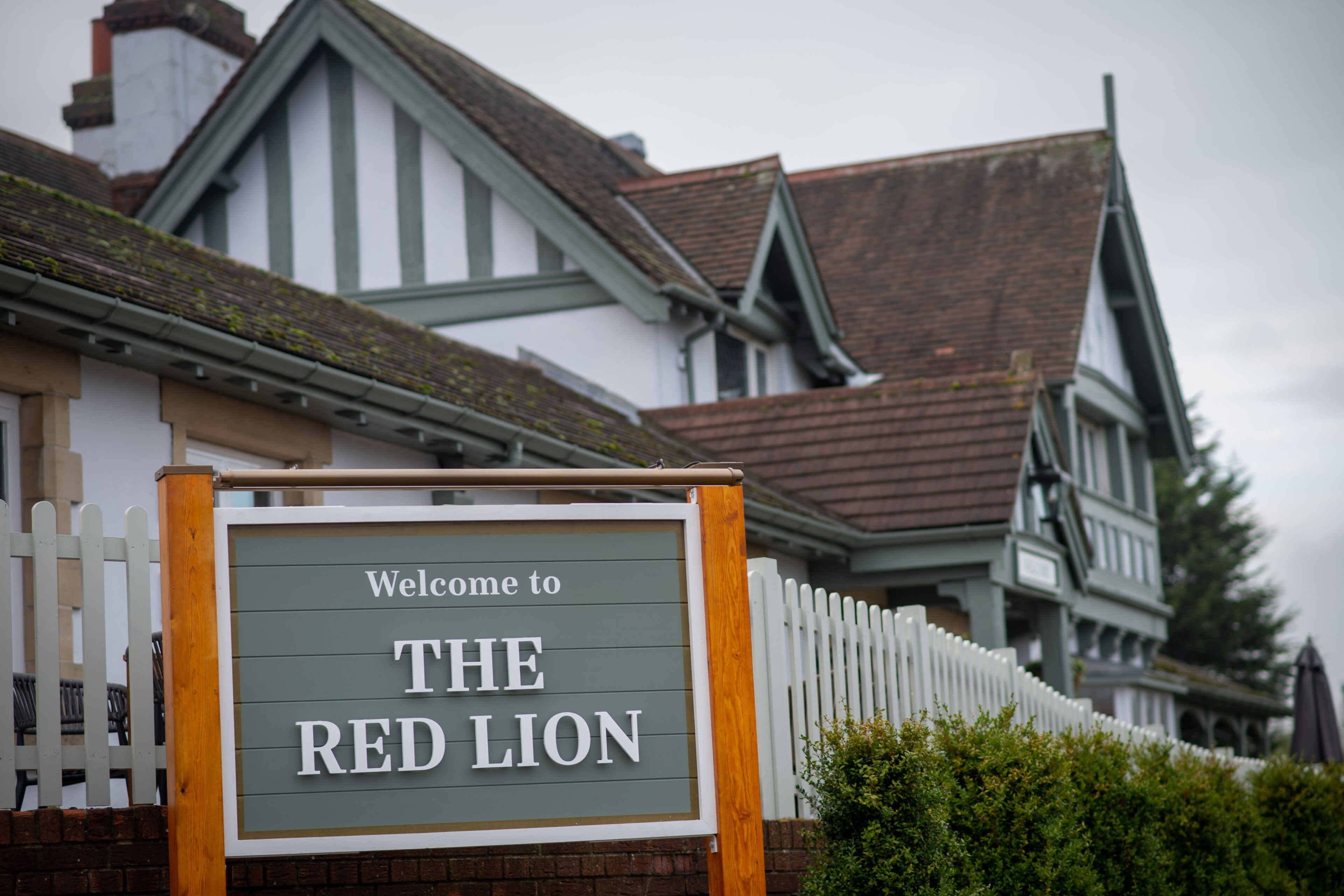 Une enseigne accueillant les visiteurs du Red Lion, un bâtiment traditionnel doté d’une clôture en bois peinte en blanc et d’un toit à forte pente.