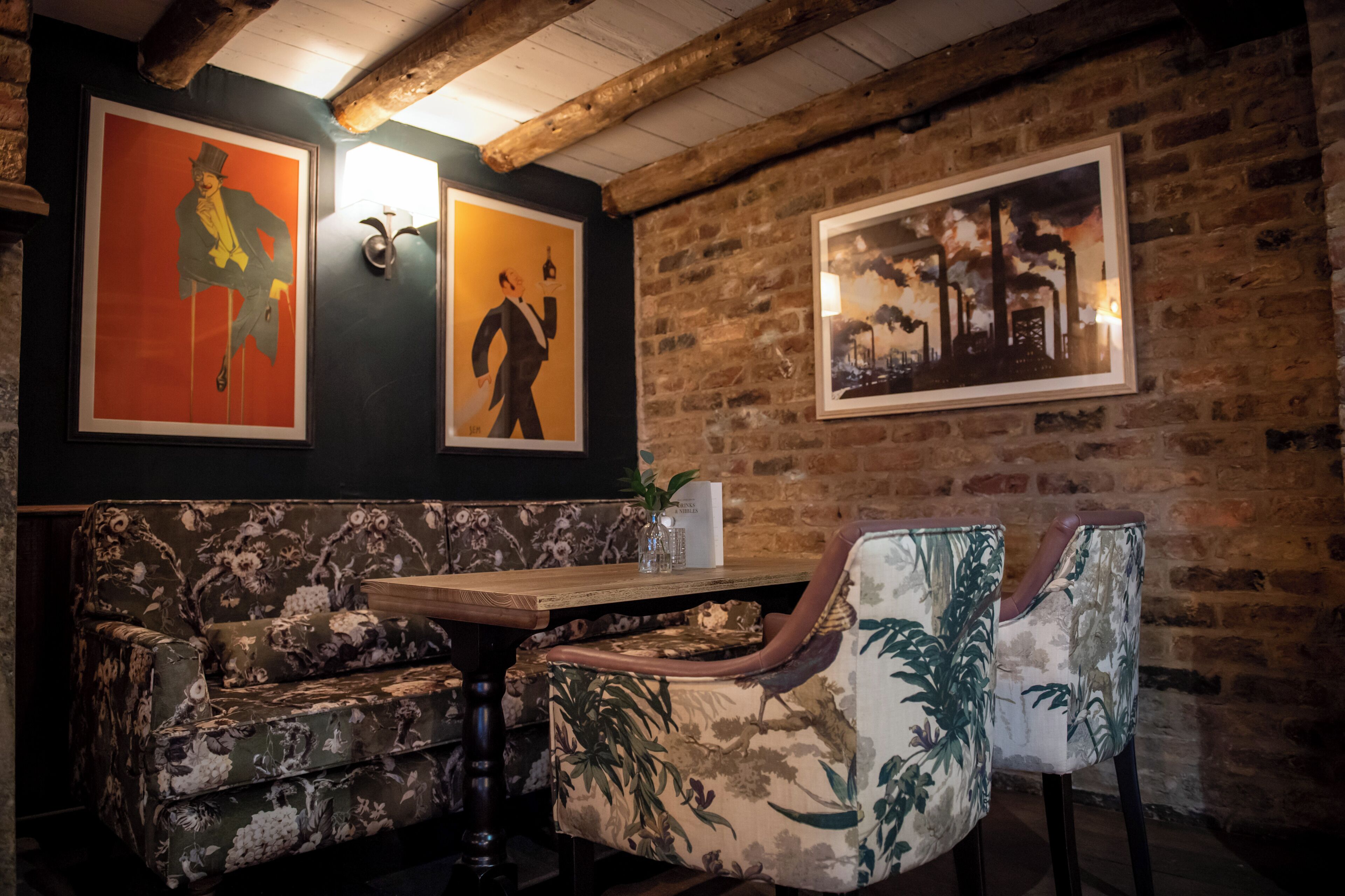 A cozy restaurant with a rustic brick wall, floral-patterned seating, and framed artwork on the wall.
