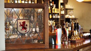 A bar area with a wooden counter, a shield with a red dragon emblem, and a variety of bottles and taps.