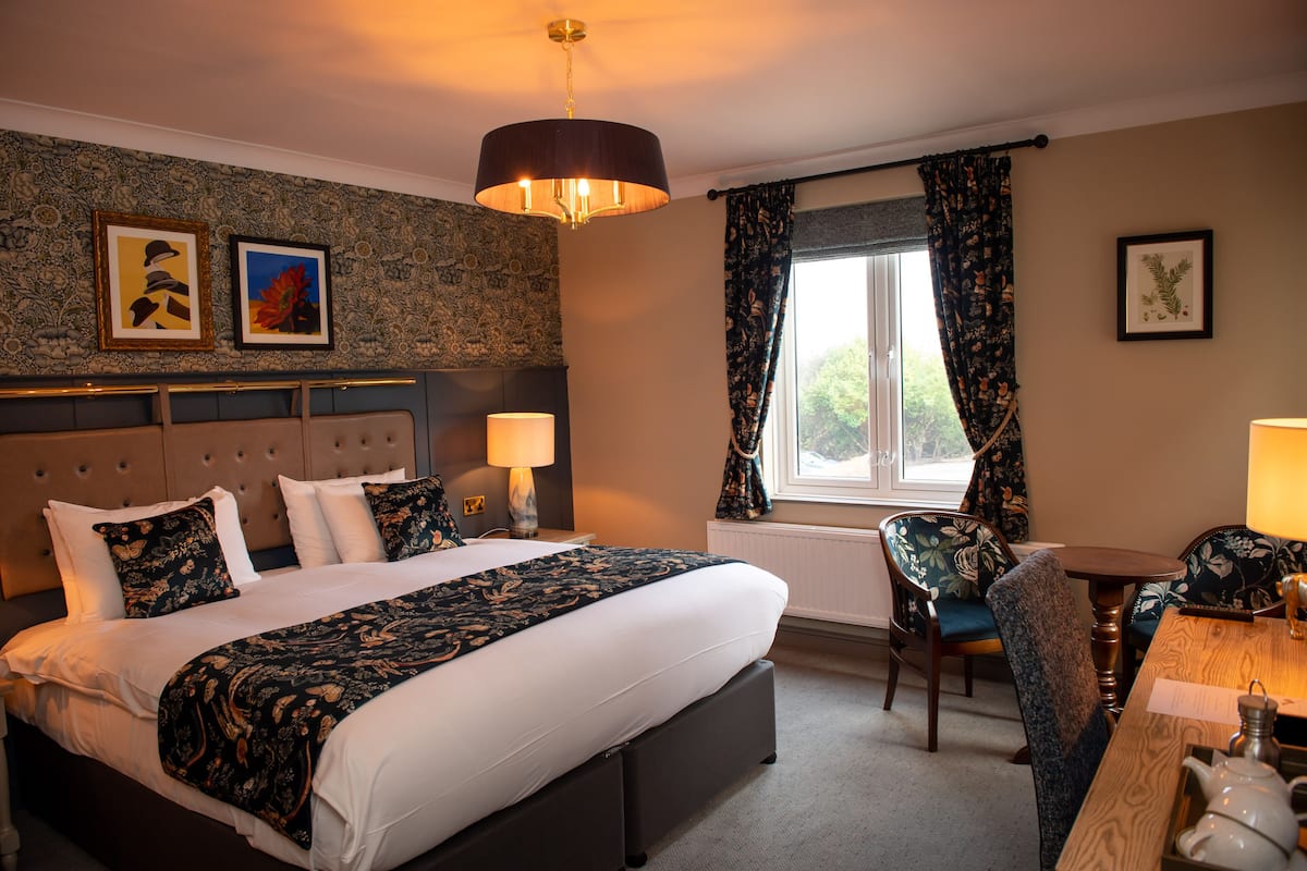 A hotel room with a large bed, two bedside tables with lamps, a wooden desk, and a chair.