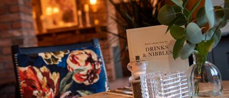 A table with a menu titled "Drinks & Nibbles" and a floral chair.