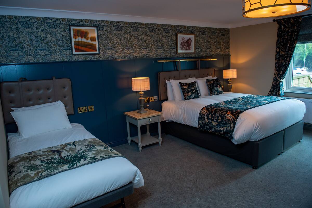 A hotel room with two beds, a nightstand with lamps, and a window with curtains.