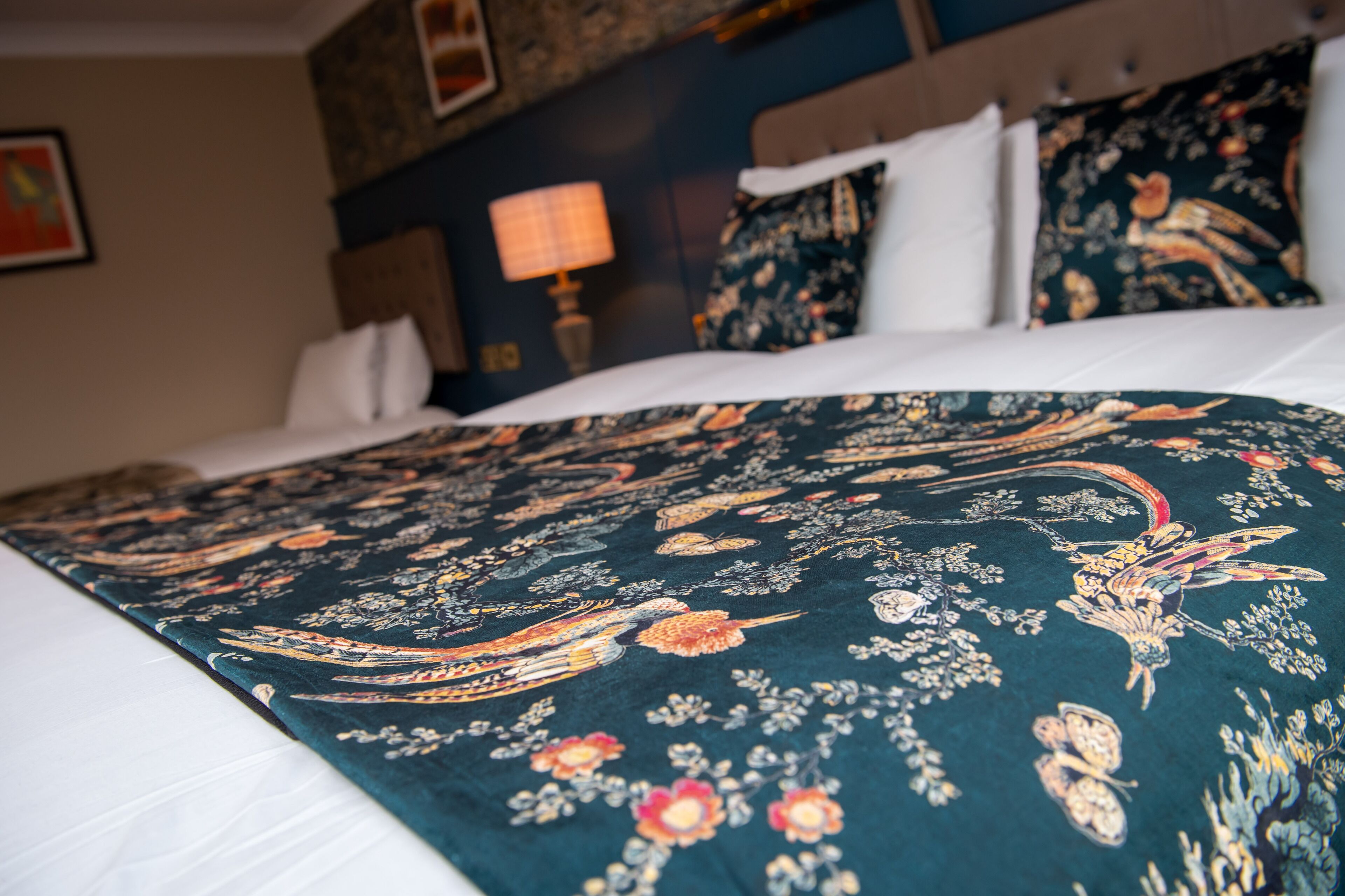 Una cama con una colcha estampada con motivos florales, cabecera y lámpara de noche.