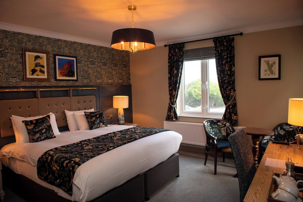 A hotel room with a large bed, a desk, a chair, and a window with curtains.
