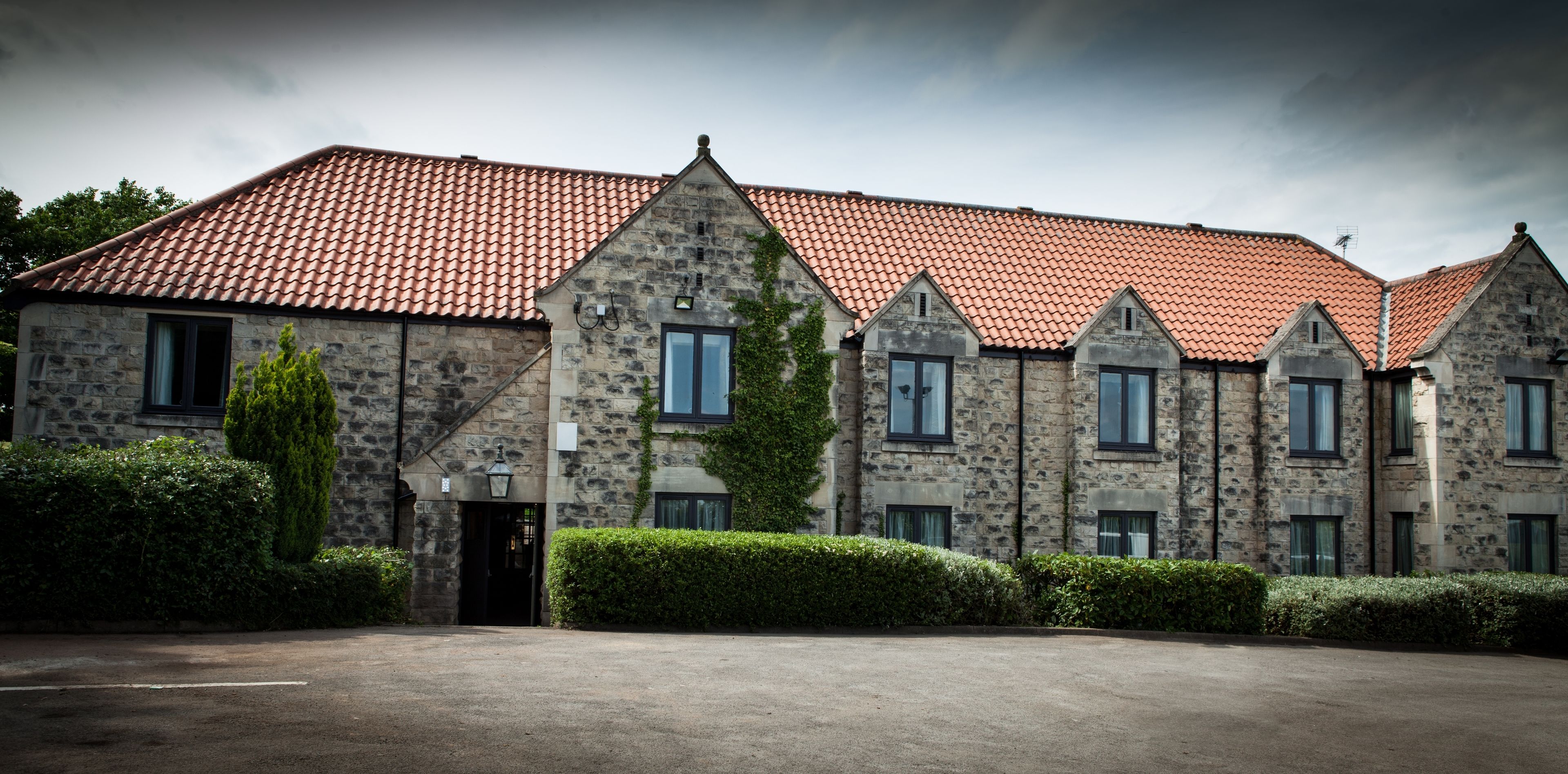 A stone building with a red-tiled roof, multiple windows, and a paved entrance area.