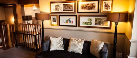 Un salon chaleureux avec un canapé foncé, deux lampes et des tableaux encadrés accrochés au mur.