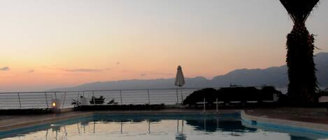 A swimming pool with a view of the sunset and mountains in the background.