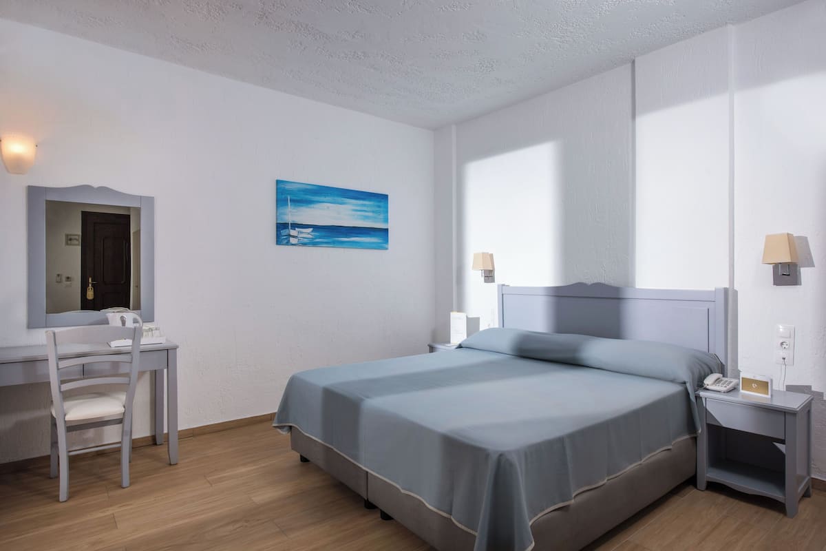 Un dormitorio con cama, escritorio, silla, mesita de noche y lámpara de pared.