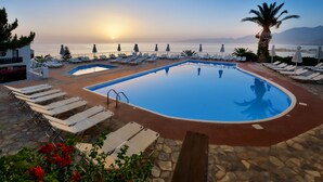 Un espace aménagé au bord de la piscine, avec des chaises longues et une vue sur la mer au coucher du soleil.