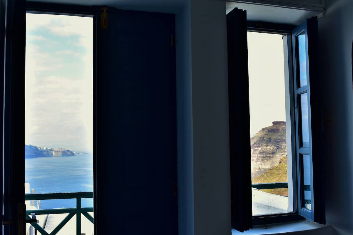 Two open windows with a view of the sea and cliffs.