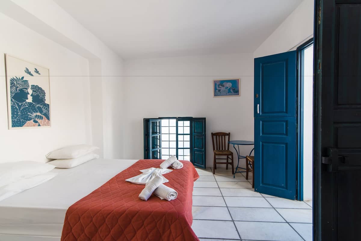 A hotel room with a bed, a chair, a table, and a blue door.
