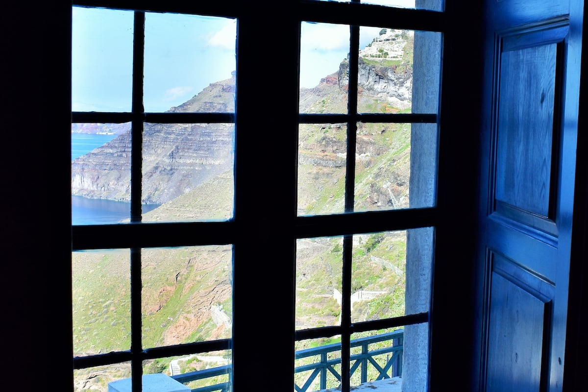 A window with a view of a mountainous landscape and a building with a blue railing.