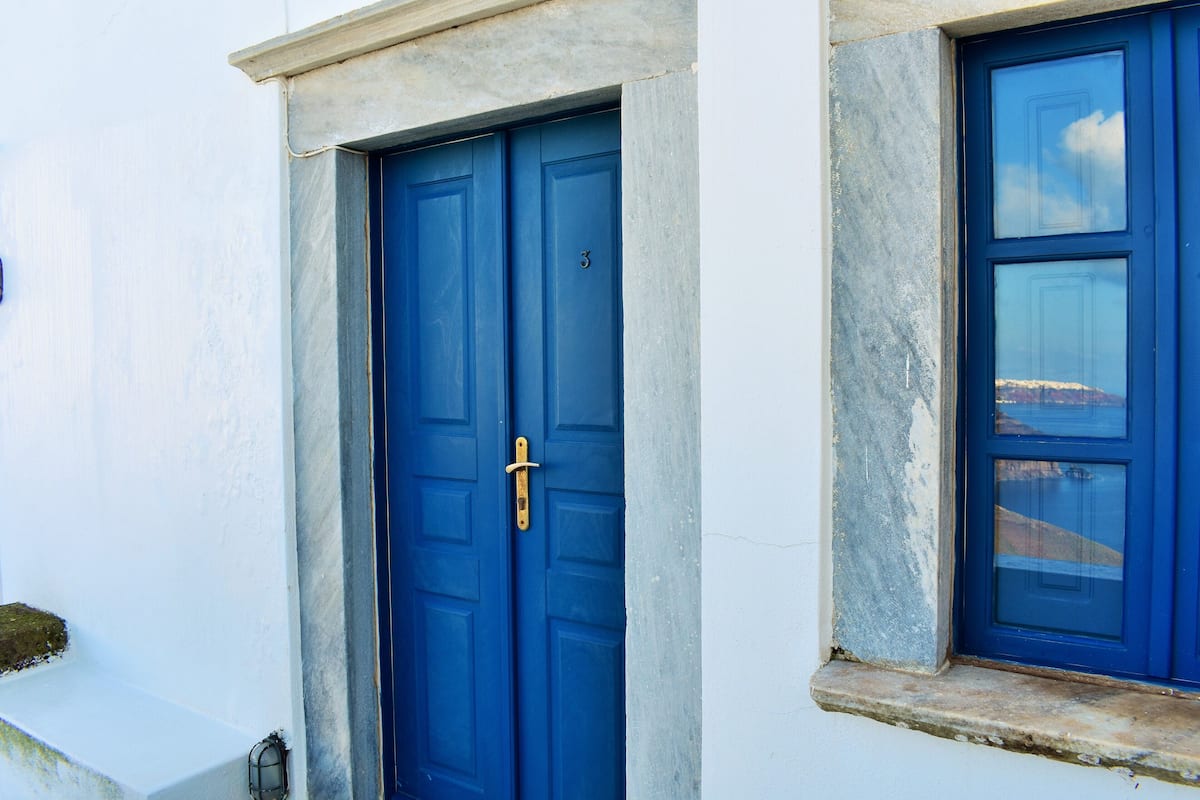 A blue door with a brass handle, set in a white building with a stone base.
