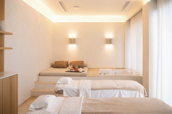 A hotel room with a sofa bed, a small table with a tray of items, and two separate beds with towels.