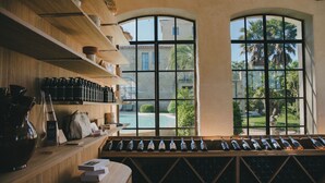 A wine cellar with shelves of bottles, a wooden counter, and a view of a pool and palm trees through large arched windows.
