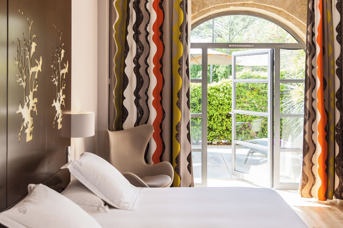Une chambre moderne avec un lit, une chaise et une vue sur l’extérieur, visible à travers une porte vitrée.