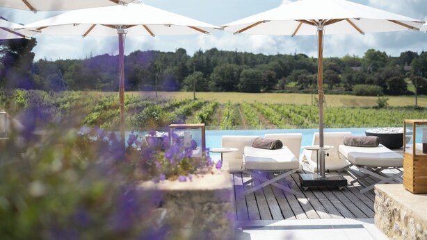 A deck with outdoor seating, umbrellas, and a view of a vineyard.