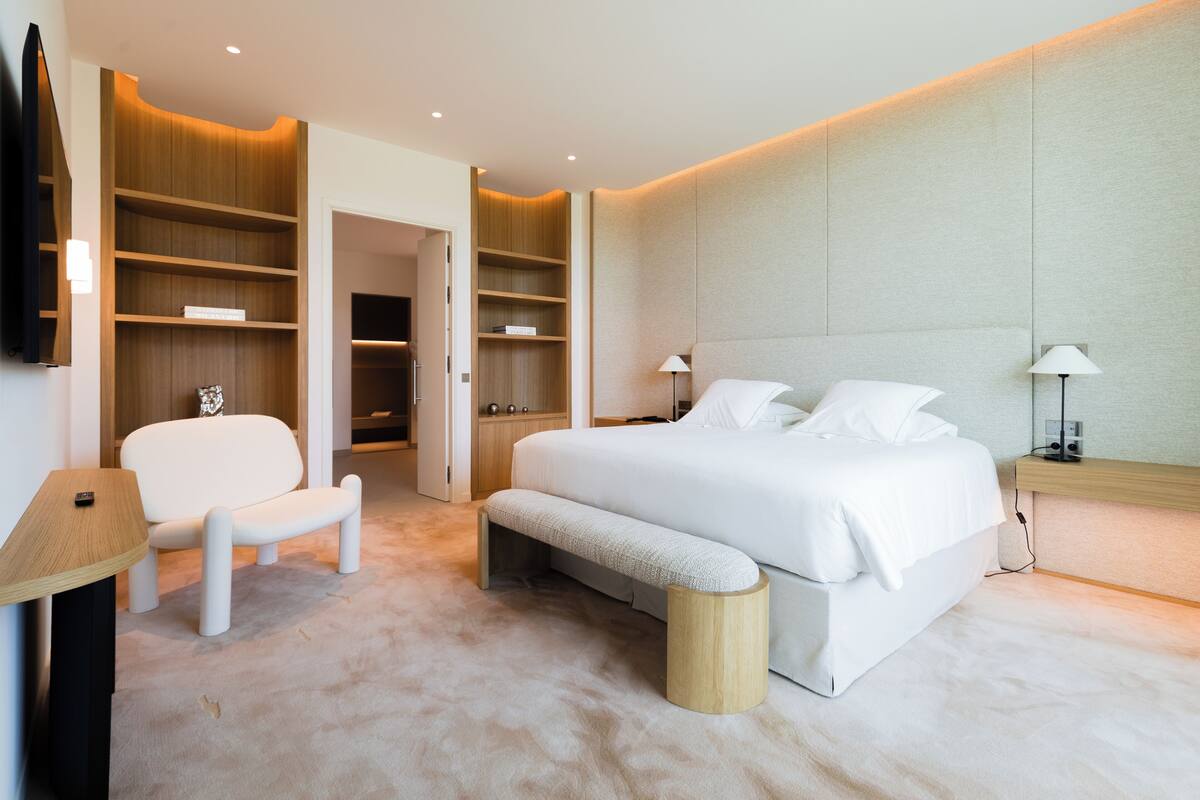 Een moderne slaapkamer met een groot bed, een bankje, een stoel en inbouwplanken.