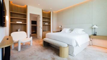 Quarto moderno com cama grande, um banco, uma cadeira e estantes embutidas.
