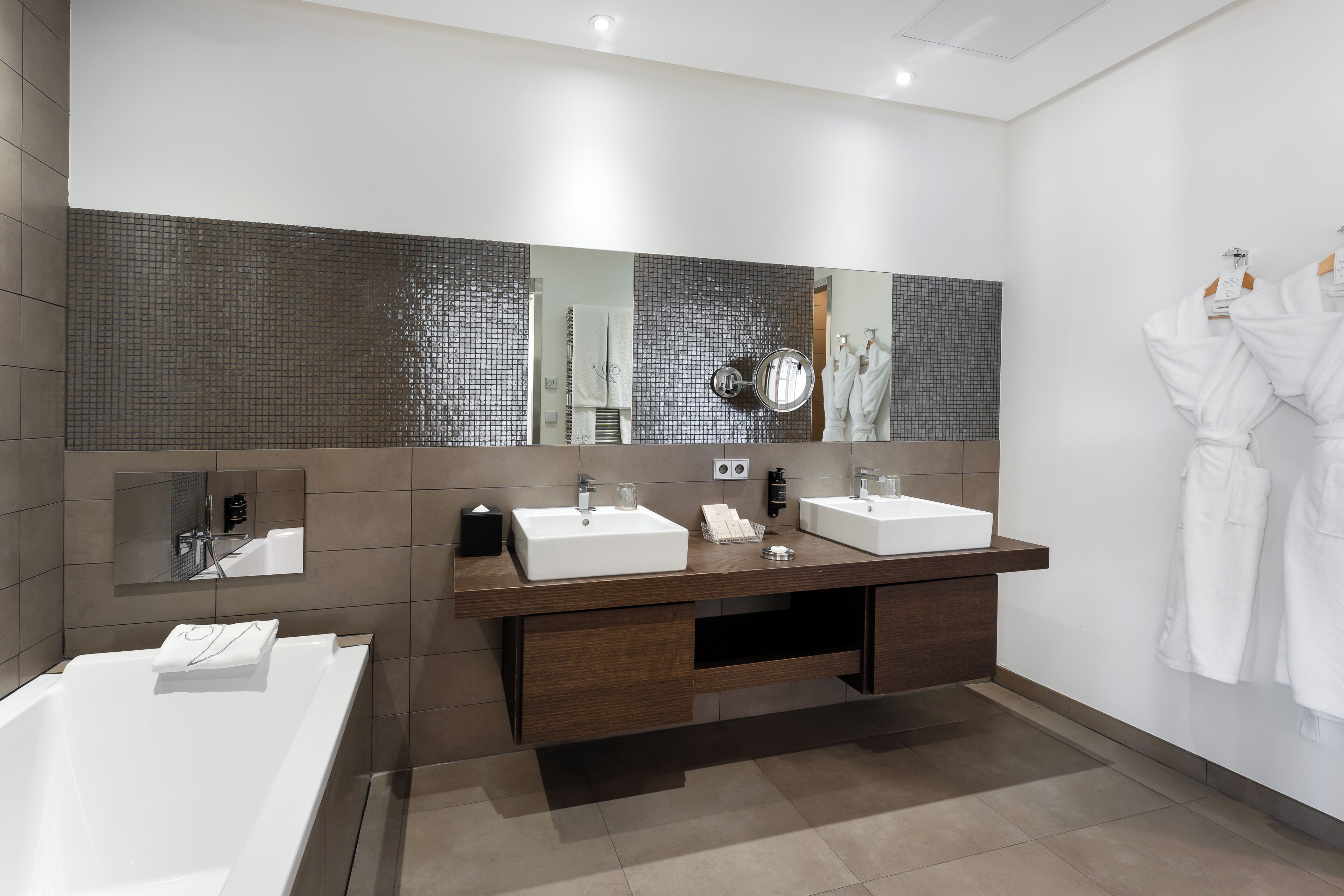A modern bathroom with two sinks, a large mirror, and a bathtub.