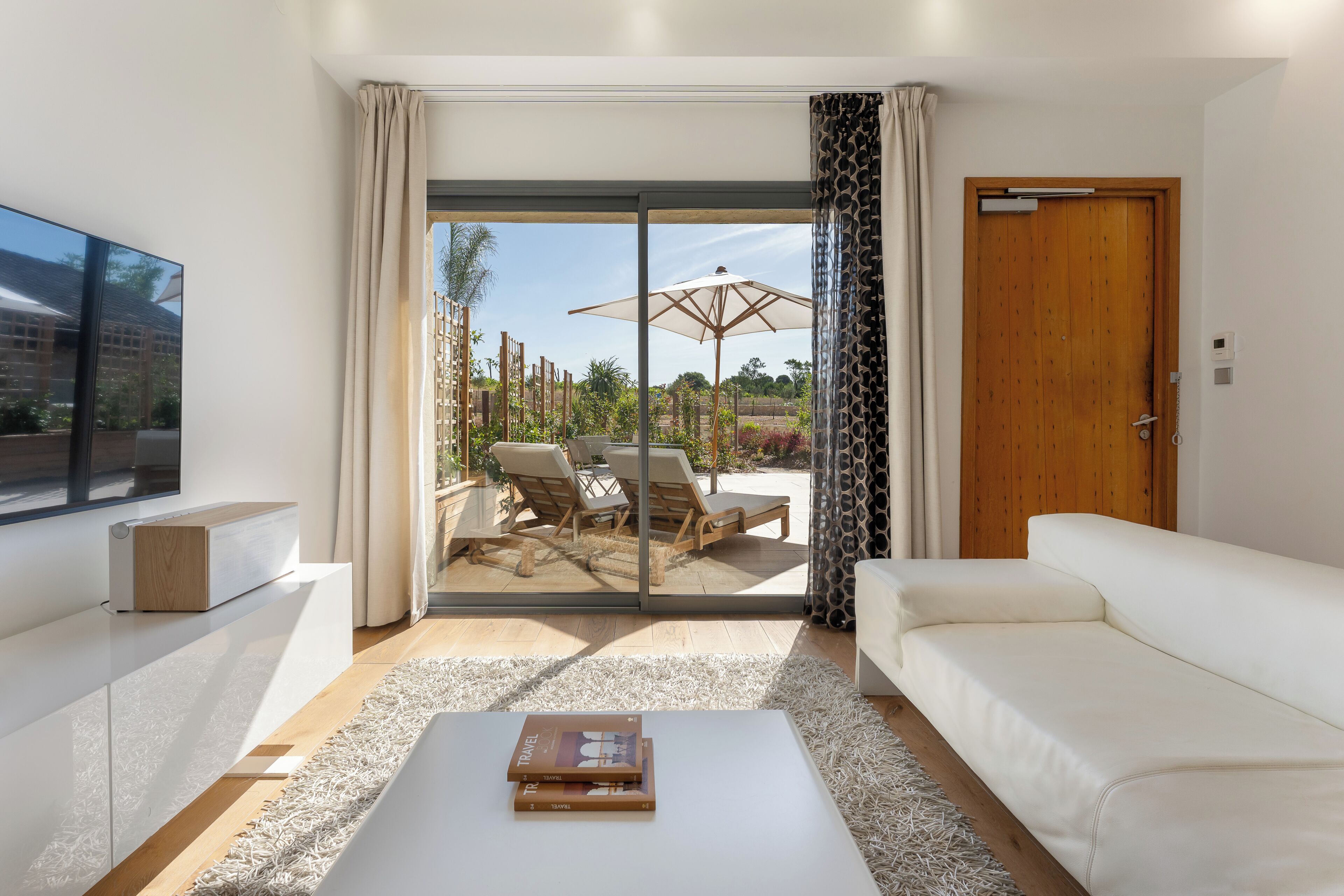 A modern living room with a white sofa, a coffee table, and a sliding glass door leading to an outdoor patio with a table and chairs.