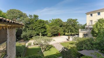 A courtyard with a stone building, a paved area, and various trees and shrubs.