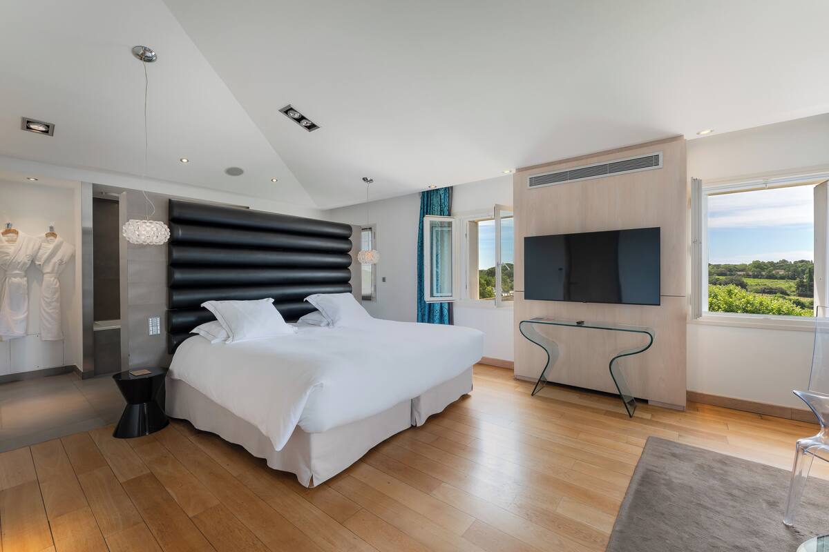 Een moderne slaapkamer met een groot bed, een televisie en uitzicht op groen.
