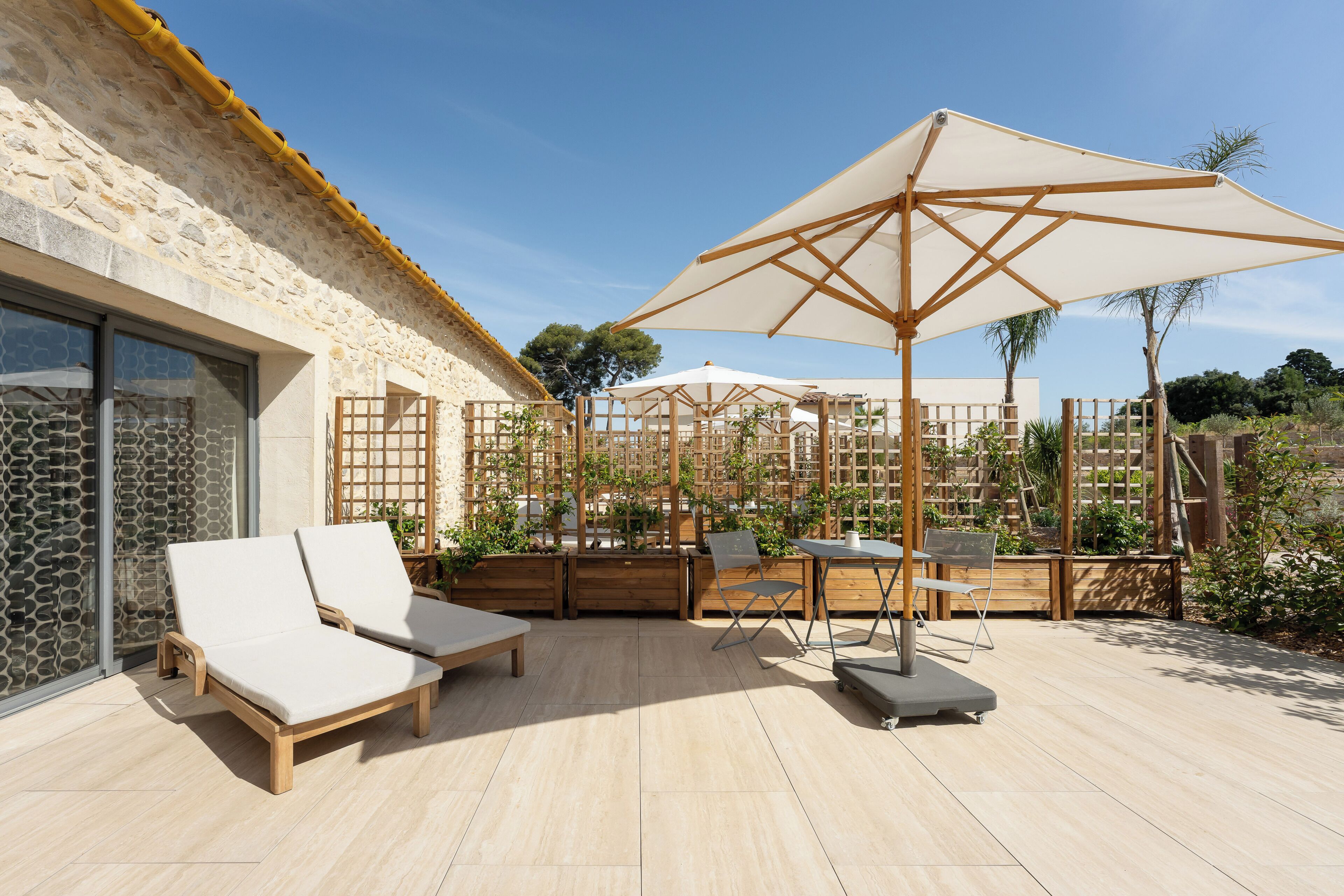 Une terrasse avec des chaises longues, une table et des parasols.