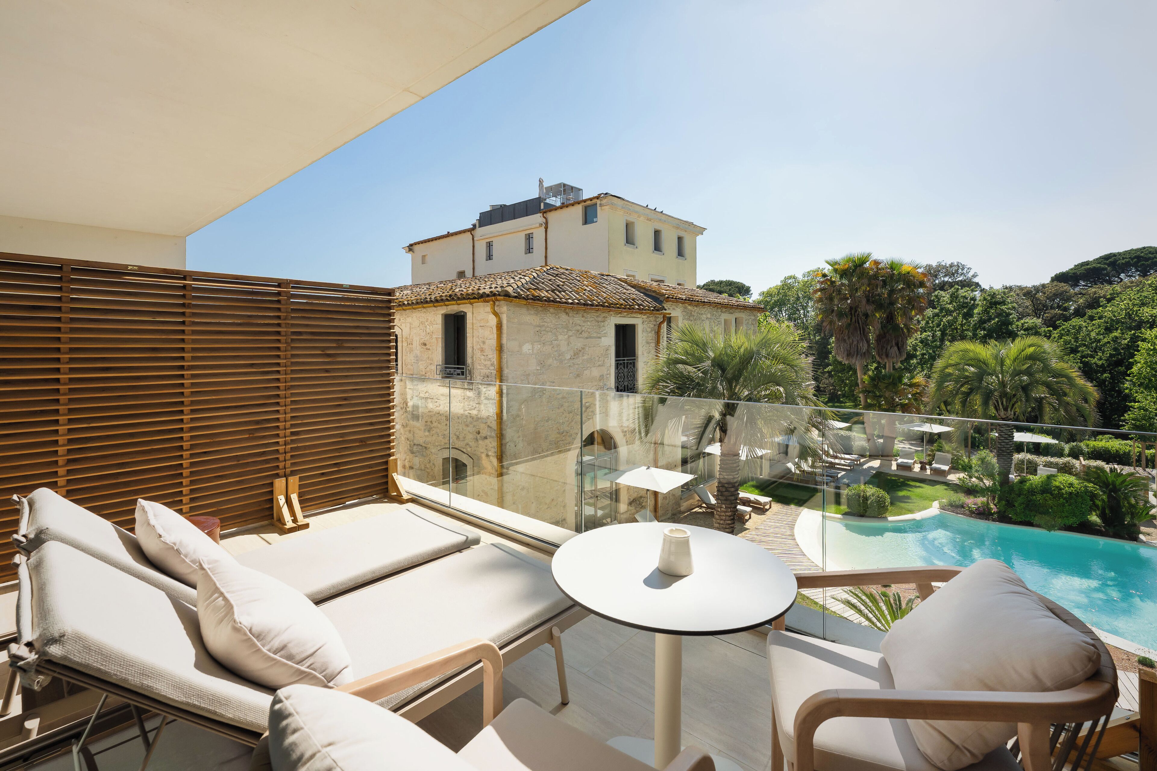 Ein Balkon mit Liegestühlen, einem Tisch und Blick auf ein Schwimmbad und Grünflächen.