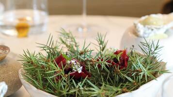 A white bowl with green foliage and red berries on a table, a glass of white wine, and a blurred background with a person.