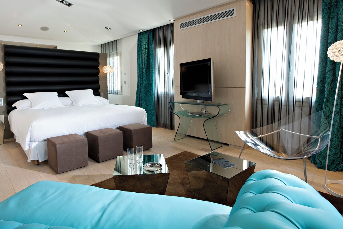 Una habitación de hotel moderna con una cama grande, un televisor, una mesita de vidrio y un sofá.