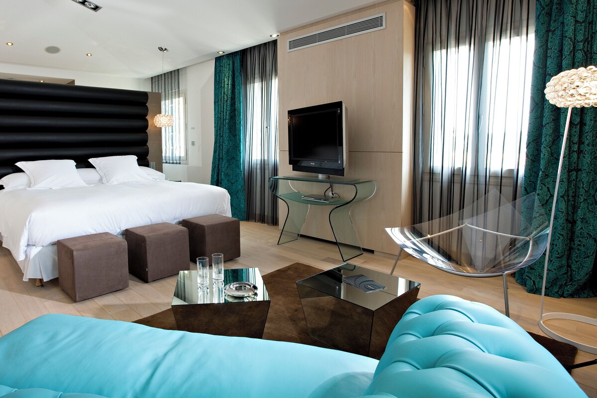 Ein modernes Hotelzimmer mit einem großen Bett, einem Fernseher, einem Glastisch und einer Couch.