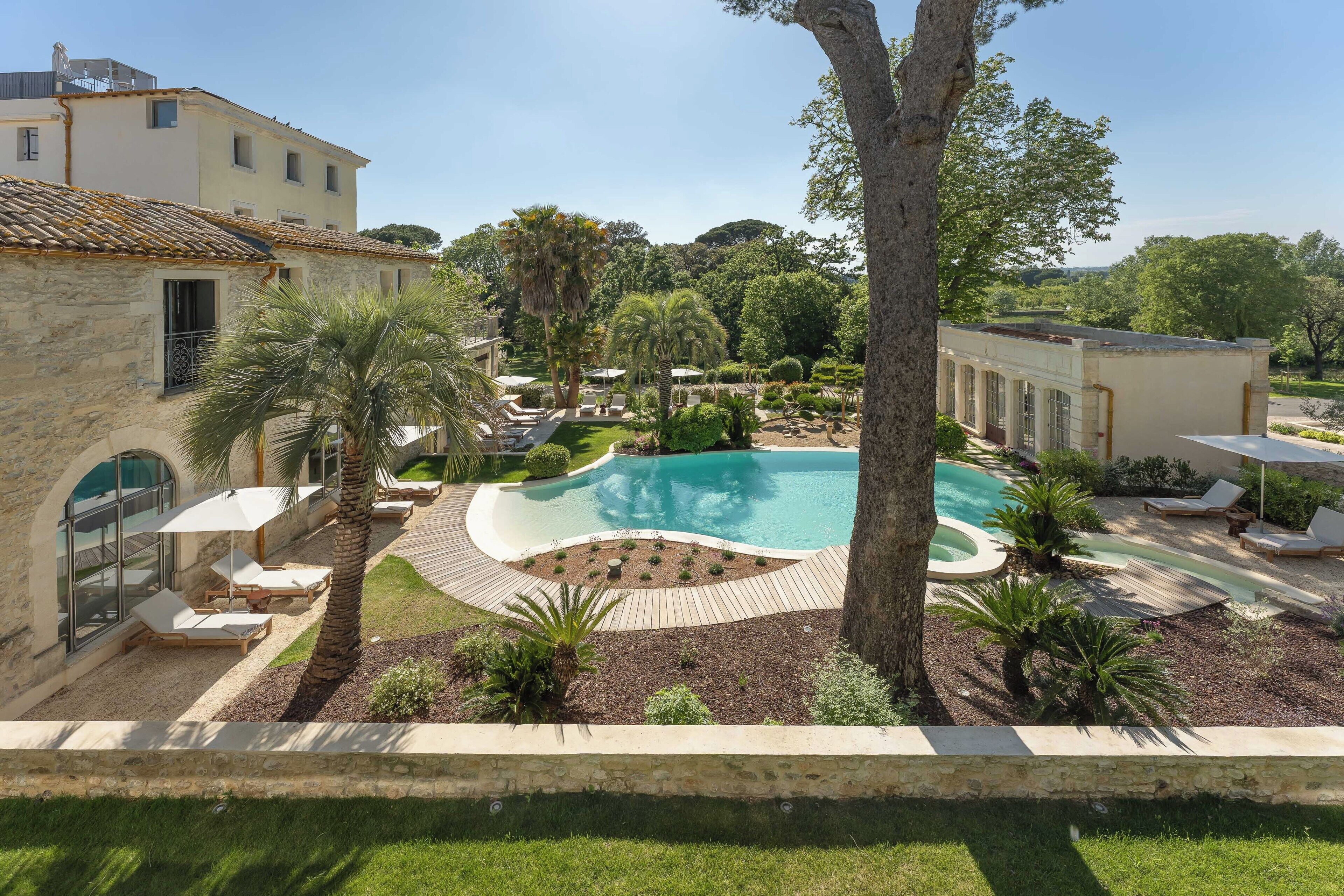 Ein Pool, umgeben von Liegestühlen, ein Steinhaus und ein angelegter Garten.