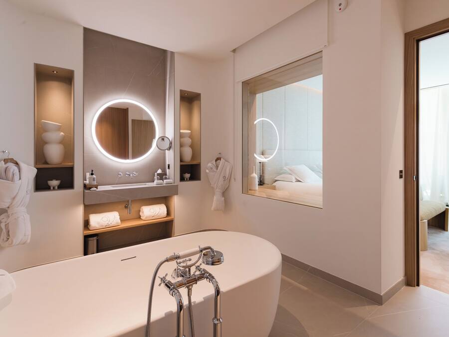 A modern bathroom with a freestanding bathtub, built-in shelves with toiletries, and a large mirror with integrated lighting.