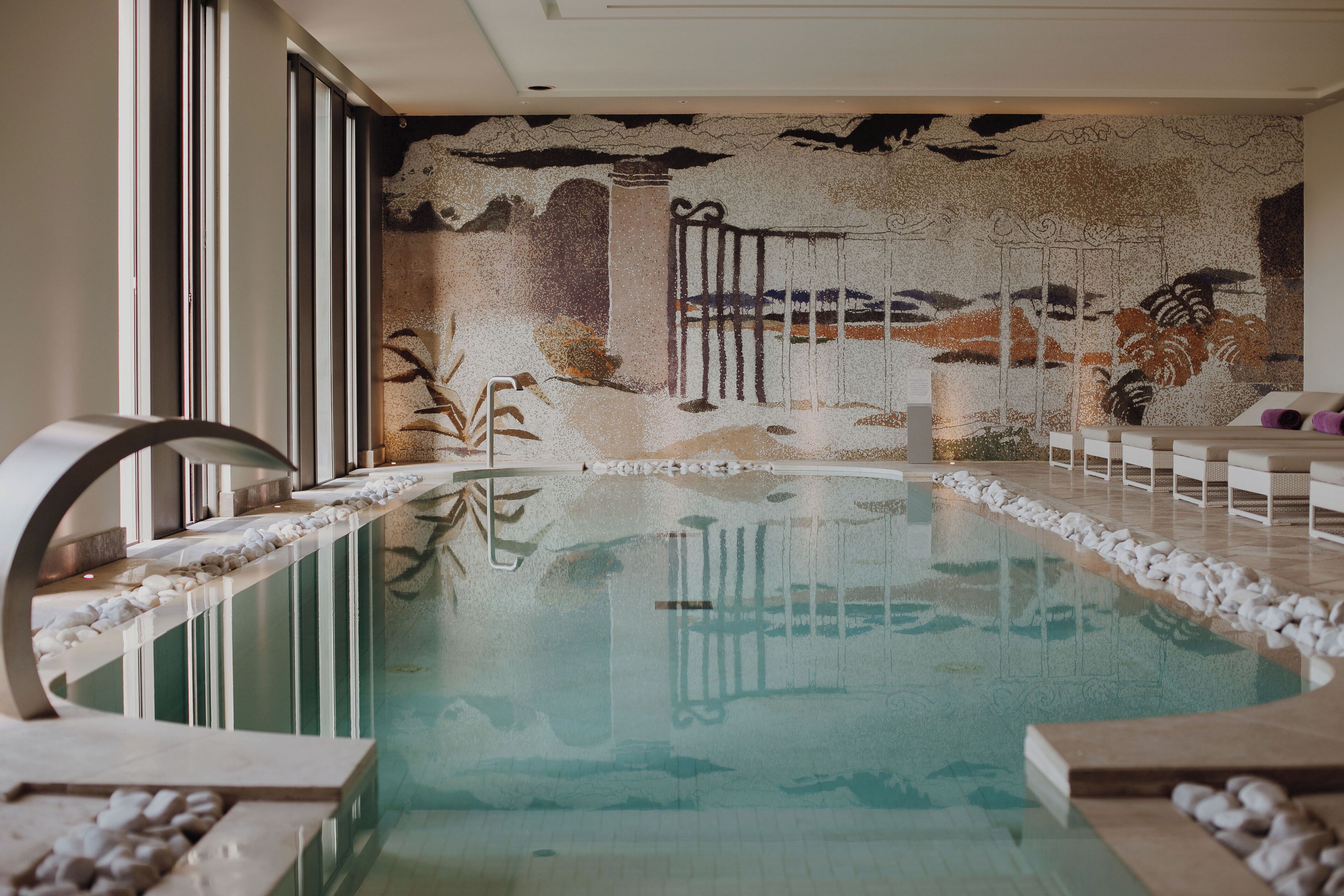 A swimming pool with a mural, stone steps, and a view of the outdoors.