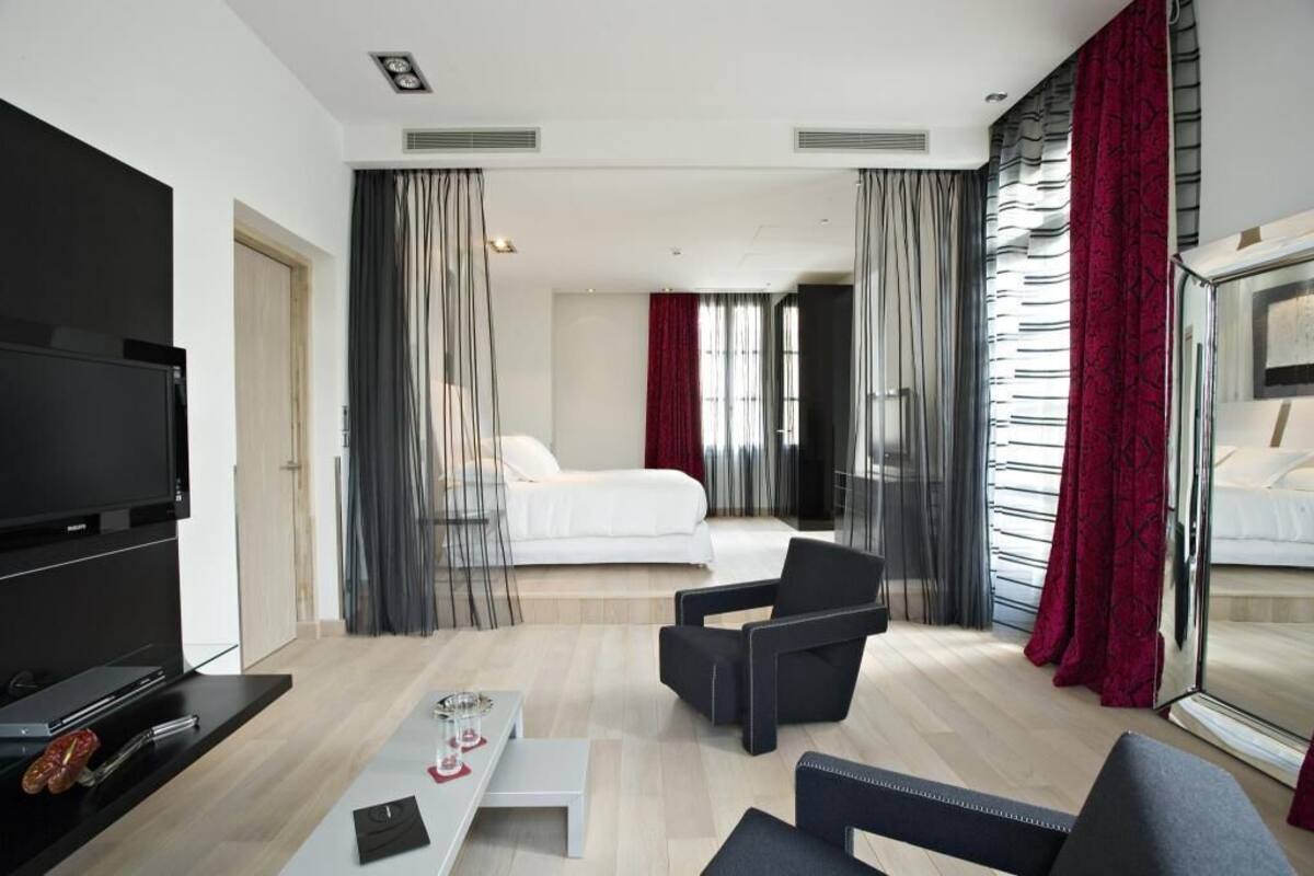 Habitació d'hotel moderna amb televisió de pantalla plana, un sofà, una taula de cafè, un llit i un mirall gran.