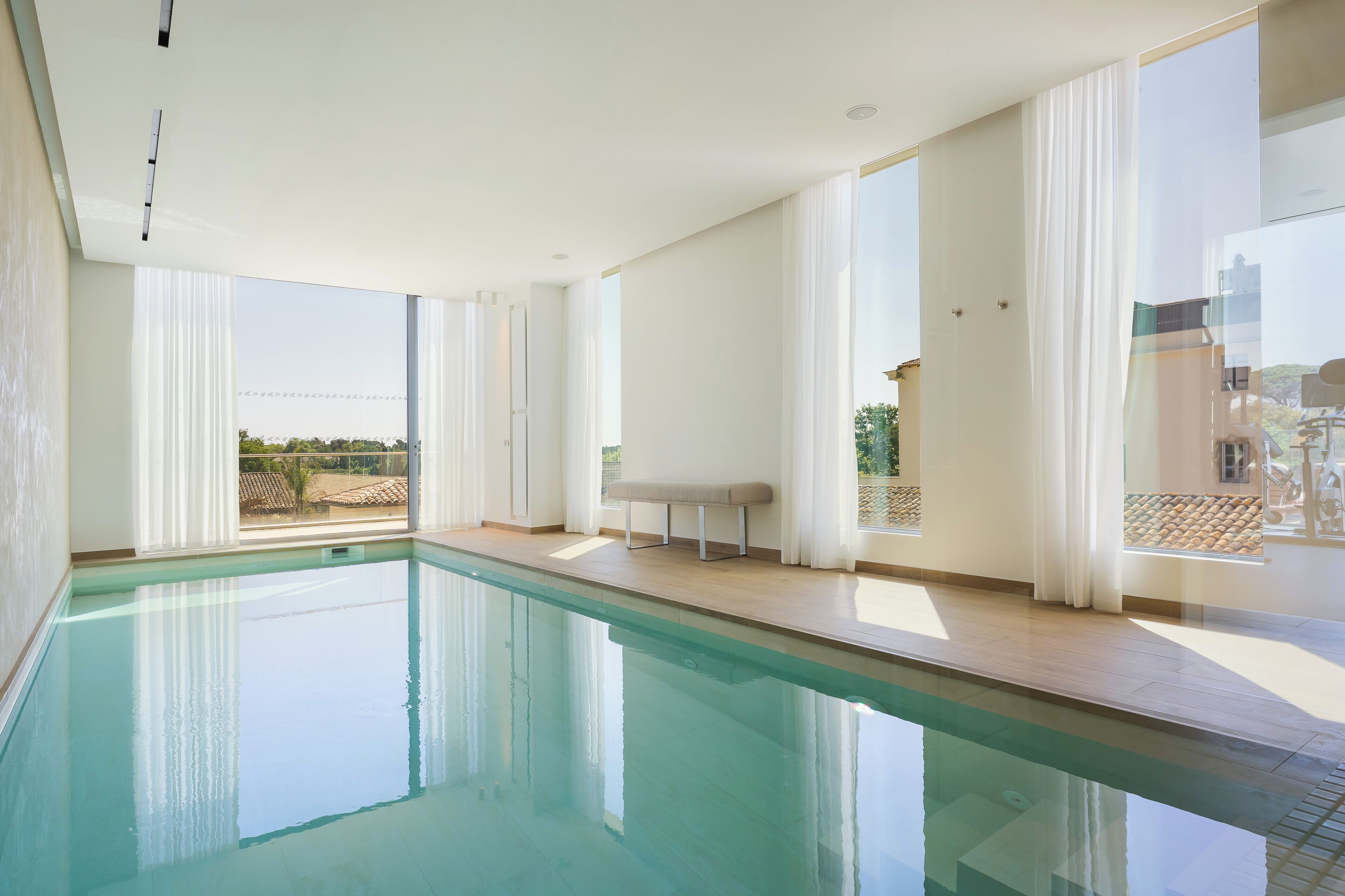 Une piscine intérieure moderne, dotée de grandes fenêtres et d’un banc.