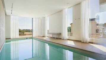 Une piscine intérieure moderne, dotée de grandes fenêtres et d’un banc.